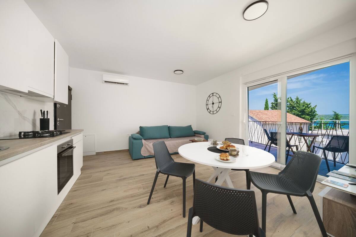 A modern kitchen with a dining area, a sofa, and a balcony with a view.