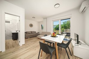 Un salon moderne comprenant un coin repas, un canapé, un téléviseur et une grande fenêtre donnant sur l’extérieur.
