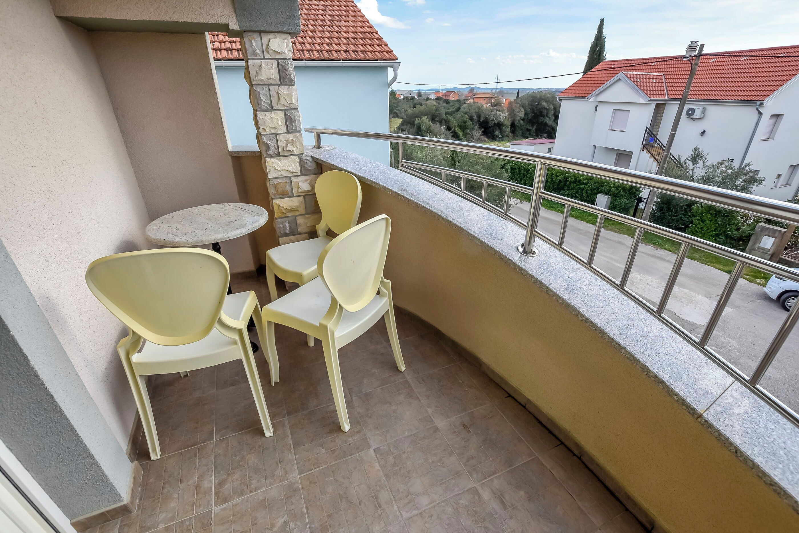 A balcony with two chairs and a small table, overlooking a residential area with houses and trees.