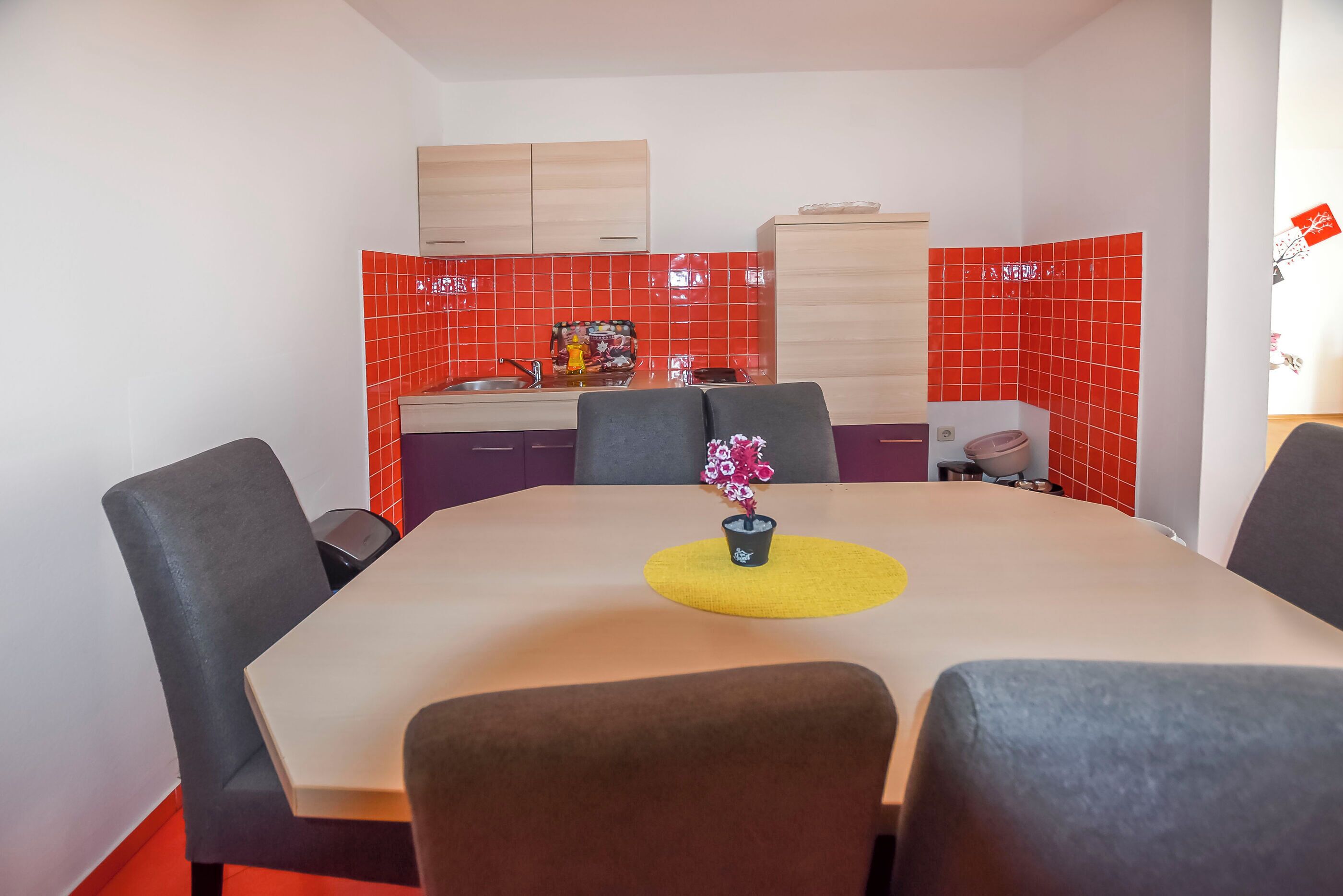 Un comedor con una mesa, sillas y una cocina al fondo.