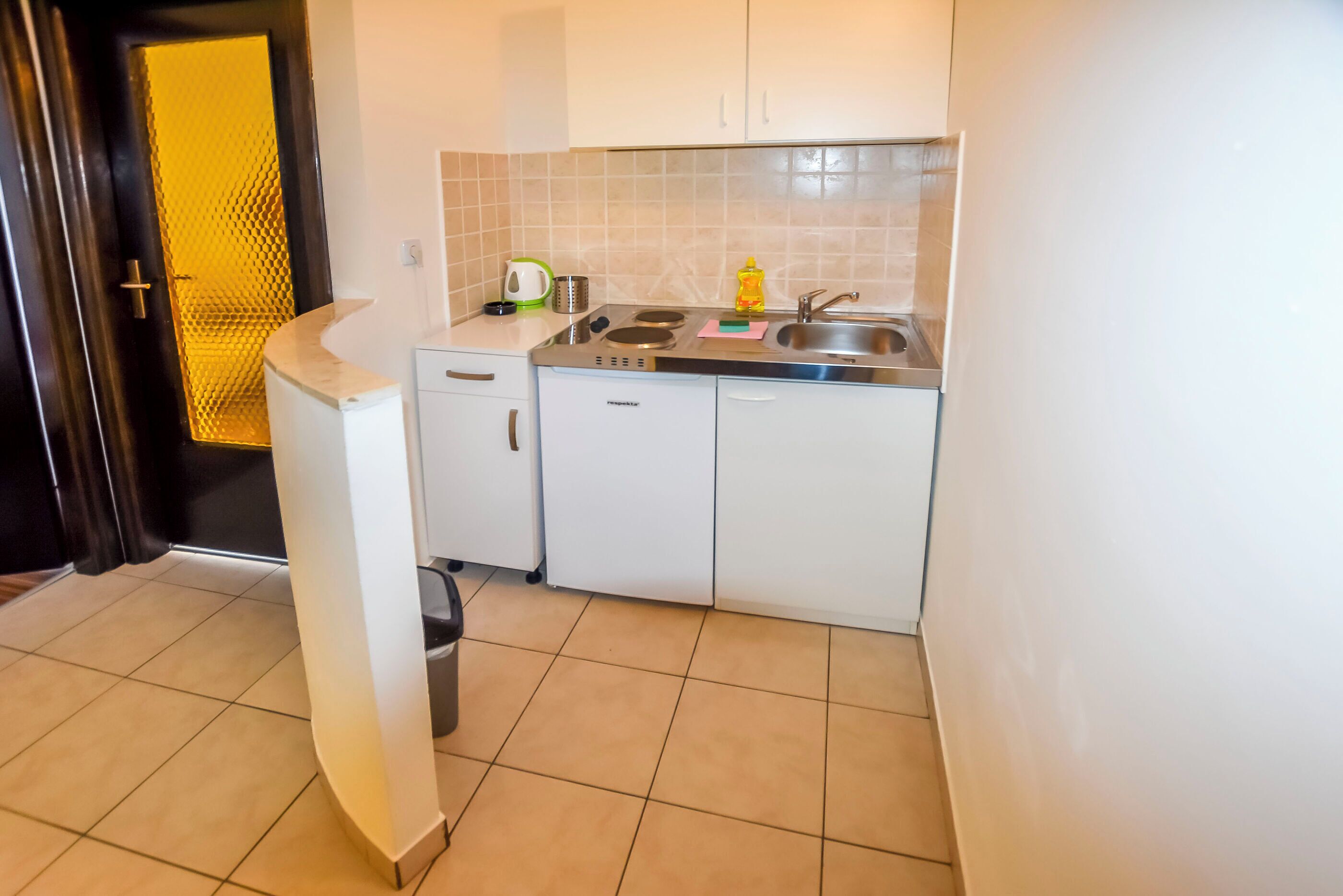Een kleine keuken met witte kastjes, een roestvrijstalen spoelbak en een klein aanrecht.