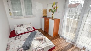 Una camera da letto con un letto, una cassettiera in legno, una finestra con tende di pizzo e vista sull'esterno.