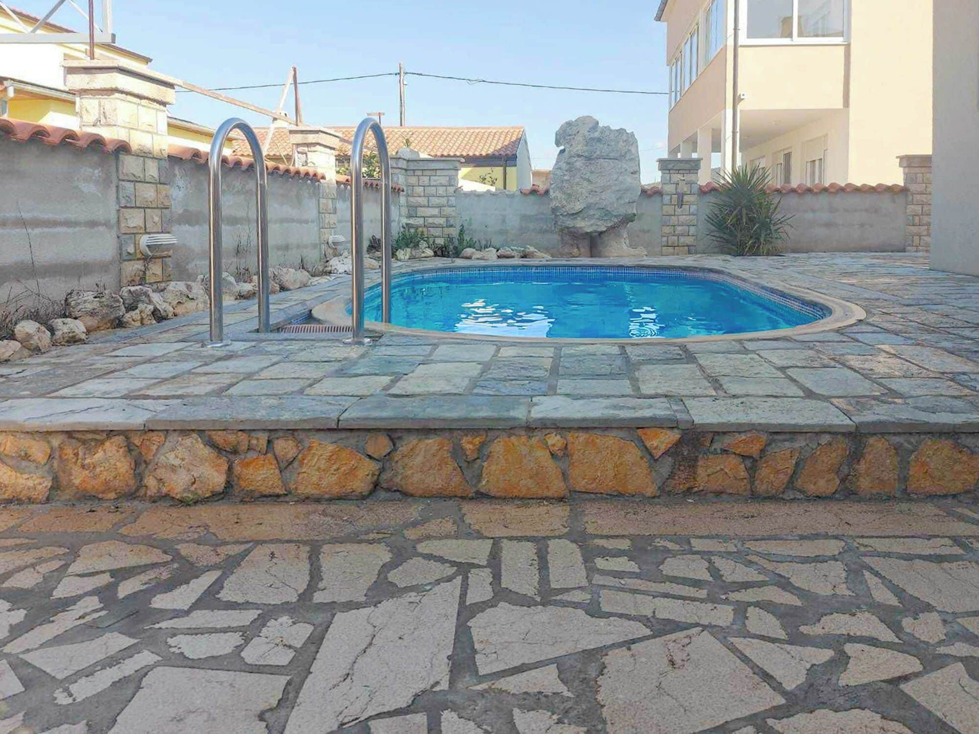 A swimming pool with stone tiles, a stone wall, and a rock feature.