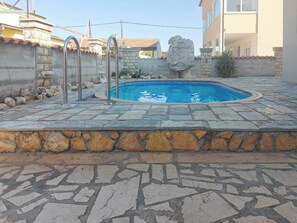 Una piscina con piastrelle in pietra, un muro di pietra e una roccia decorativa.
