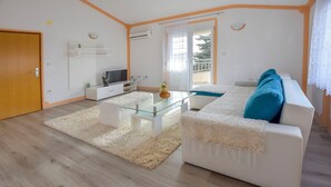 Un soggiorno moderno con un tavolino in vetro, un divano bianco e una TV su un mobile bianco.