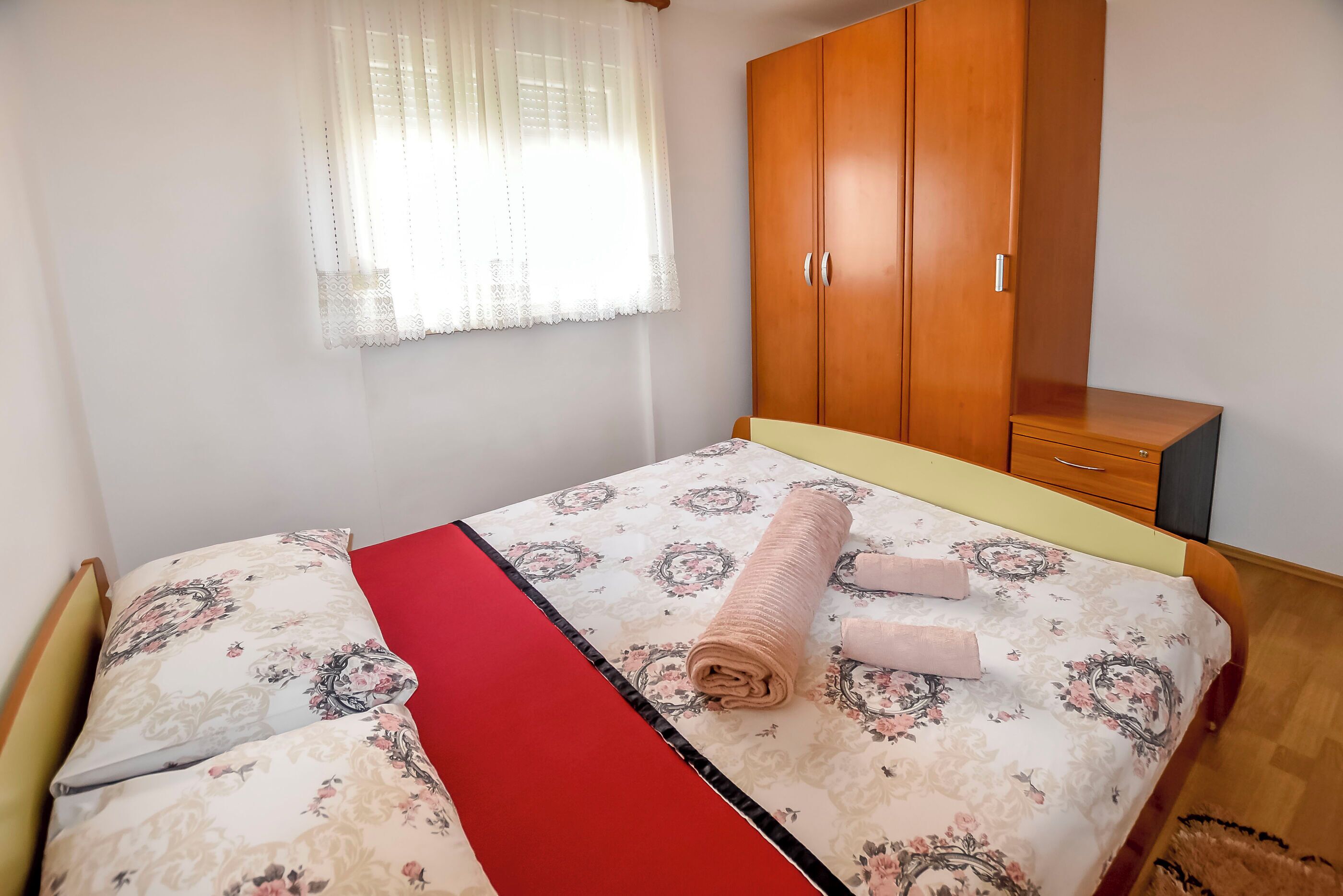 A bedroom with a bed, a wooden wardrobe, and a window with sheer curtains.