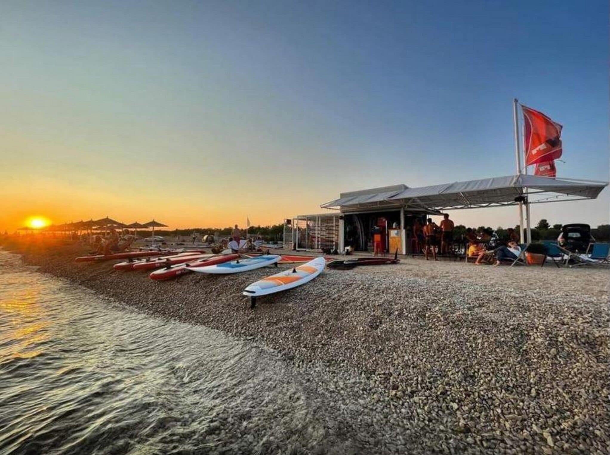Une plage où des kayaks sont alignés et une zone abritée où se trouvent des personnes.