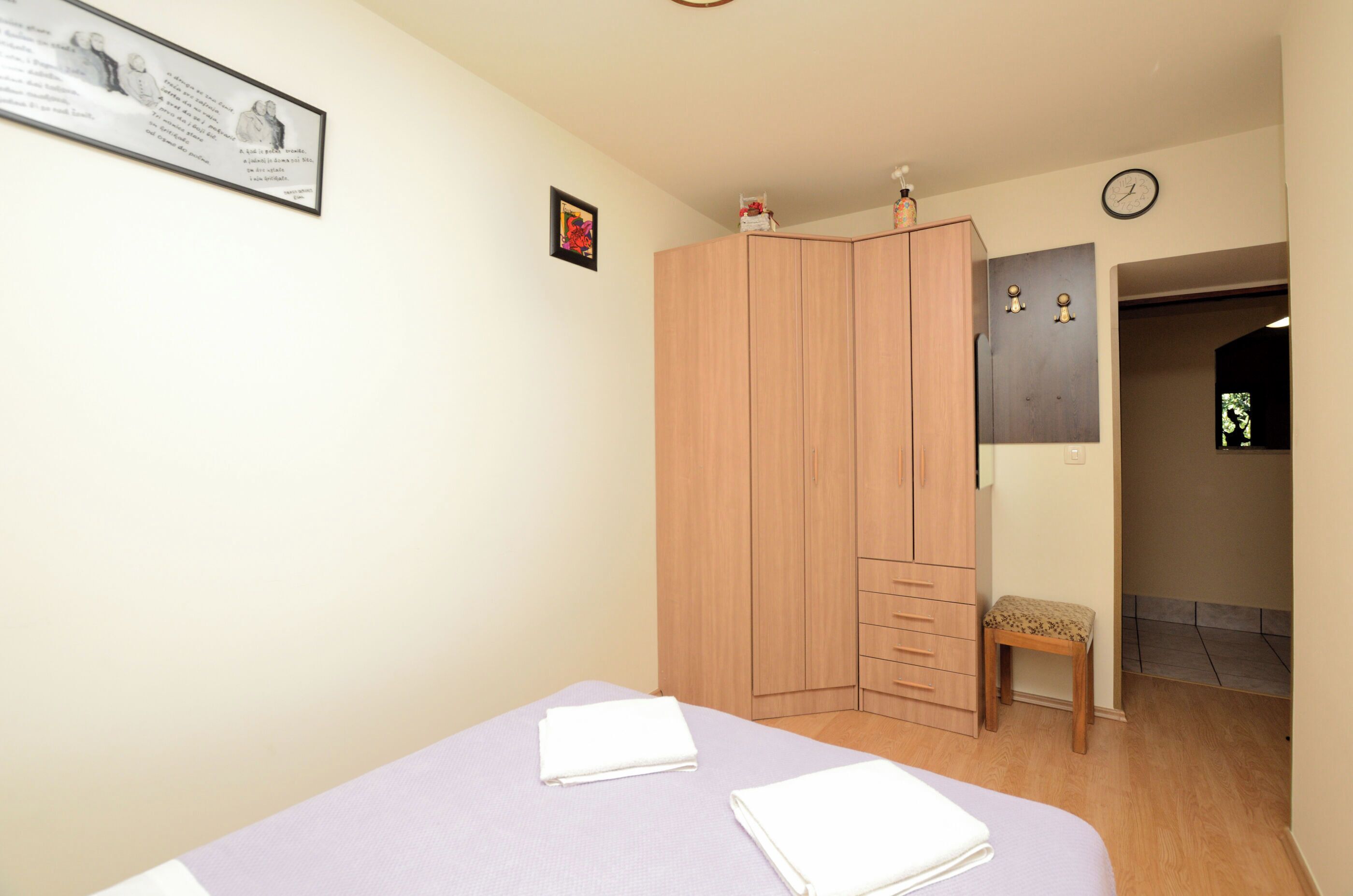 A bedroom with a bed, a wardrobe, a small stool, and a framed quote on the wall.