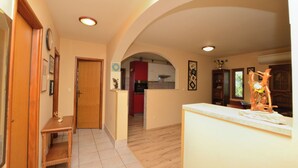 Un hall d’entrée spacieux avec une porte en bois, une petite table et un coin cuisine visible à travers une arche.