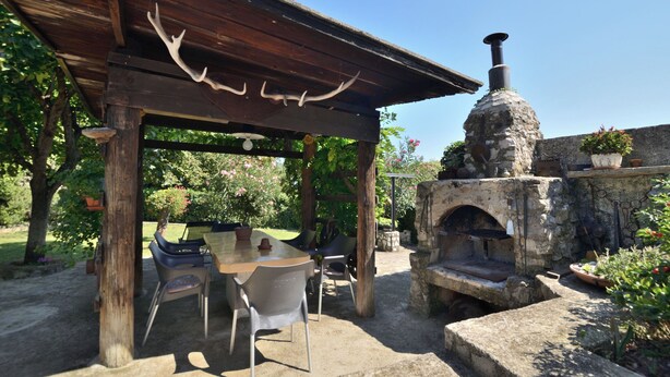 Une terrasse extérieure dotée d’un four en pierre, d’une pergola en bois et d’une table avec des chaises.