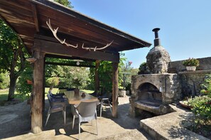 Eine Außenpatio mit Steinofen, Holz-Pergola und Tisch mit Stühlen.