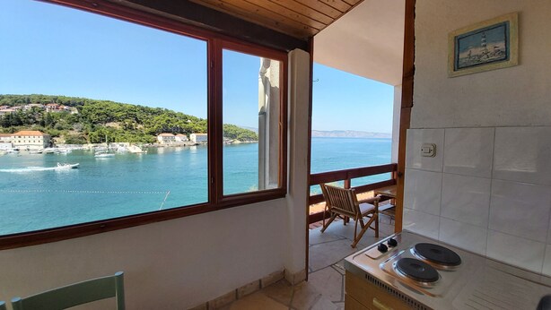 A small kitchen with a view of a coastal town, a dining area with a table and chairs, and a wooden ceiling. - Apartment Next to the sea (Jelsa)