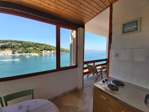 A small kitchen with a view of a coastal town, a dining area with a table and chairs, and a wooden ceiling. - Apartment Next to the sea (Jelsa)