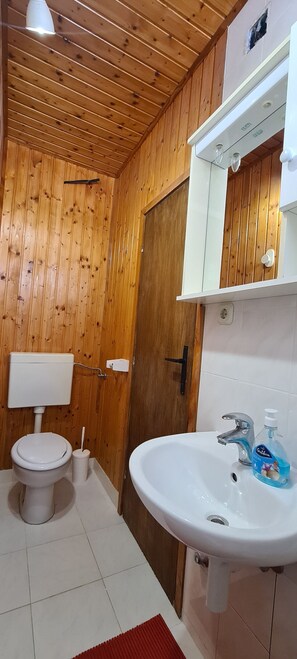 Et badeværelse med træpaneler, toilet, håndvask og en trädør.