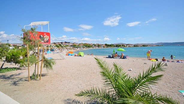A beach with a lifeguard tower, umbrellas, and people relaxing. - Apartment Mia (Sibenik)