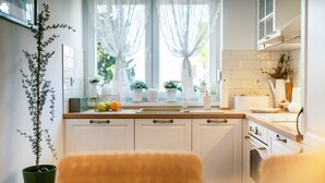 A modern kitchen with white cabinets, a wooden countertop, and a window with sheer curtains. - Apartment Mia (Sibenik)