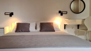 Habitación de hotel impecable con una cama grande, dos lámparas de noche, un espejo y un escritorio con una silla.