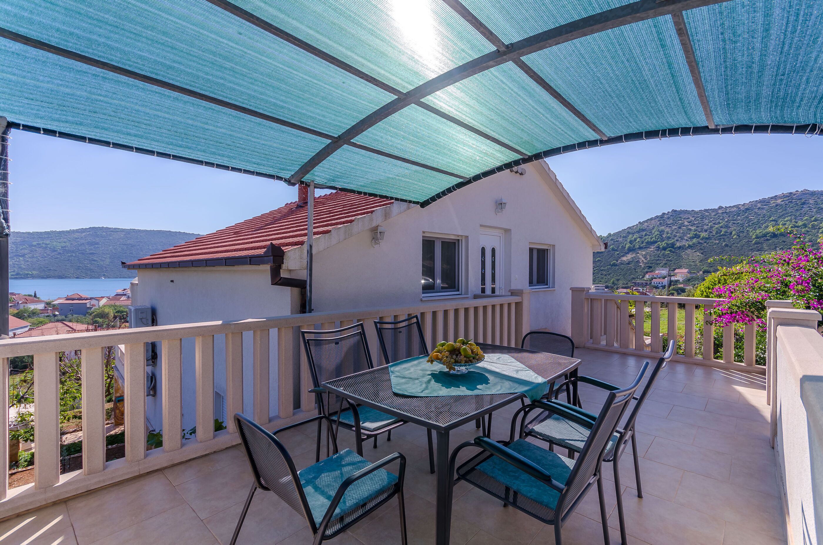 A balcony with a table and chairs, a view of the sea, and a house in the background.