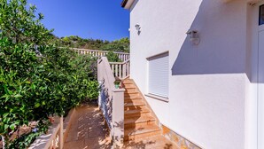 Ein weißes Gebäude mit einer Treppe, die zu einem Balkon führt, umgeben von Grünpflanzen.