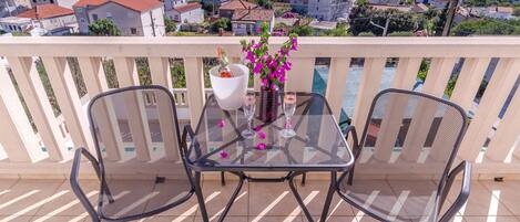 A balcony with a table and two chairs, overlooking a coastal town with houses and a body of water.