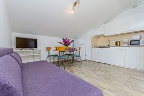 A modern kitchen with white cabinets, a dining table with chairs, a purple sofa, and a flat-screen TV on a white wall. - Apartment Karolina (Marina)