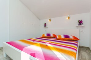 A modern bedroom with a large bed, white walls, and built-in shelving with decorative items. - Apartment Karolina (Marina)