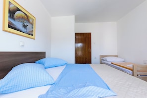 Een slaapkamer met een groot bed, een kleiner bed, een houten deur en een schilderij aan de muur.