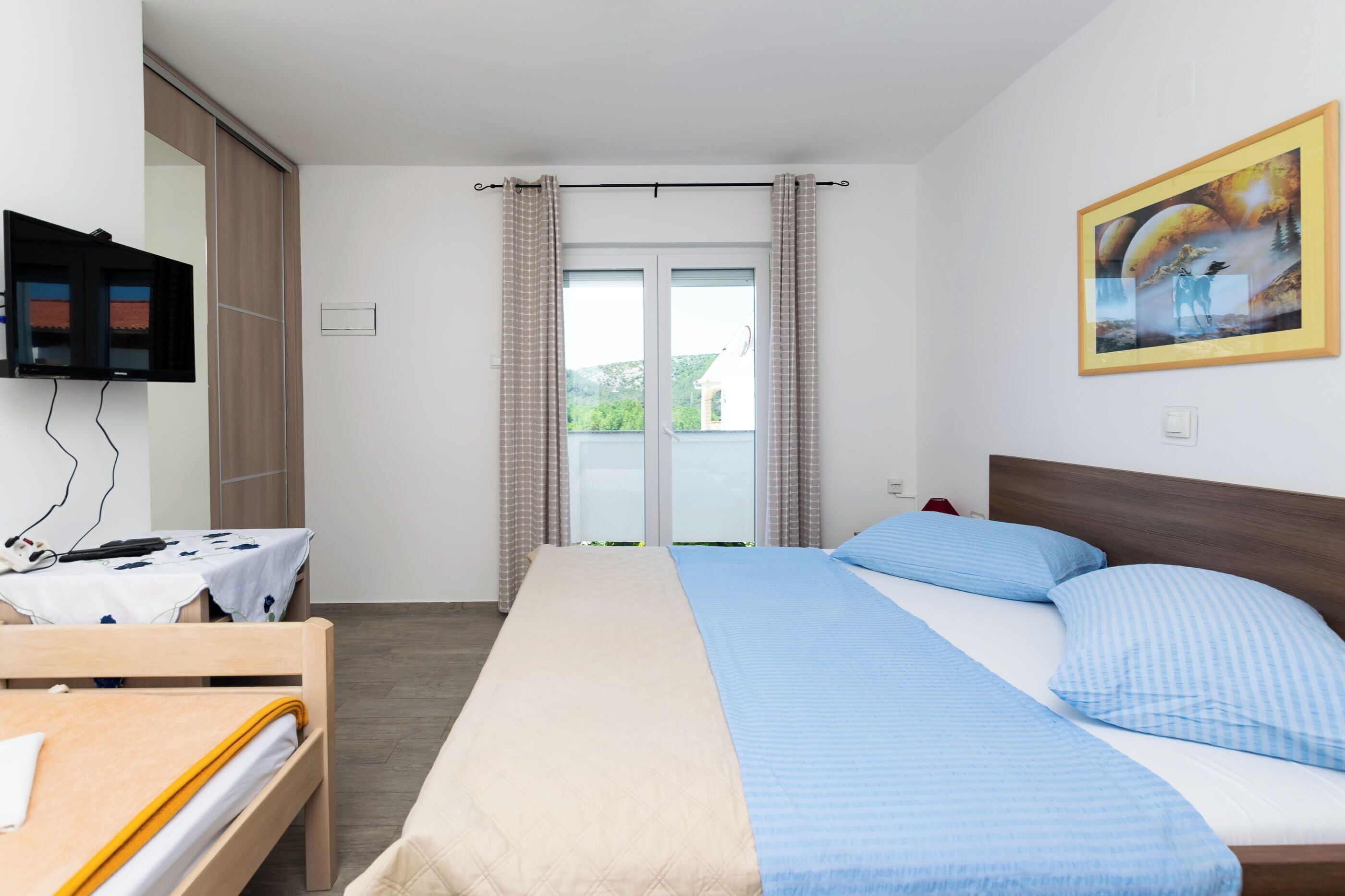 Quarto de hotel com cama, escrivaninha, televisão e janela com cortinas.