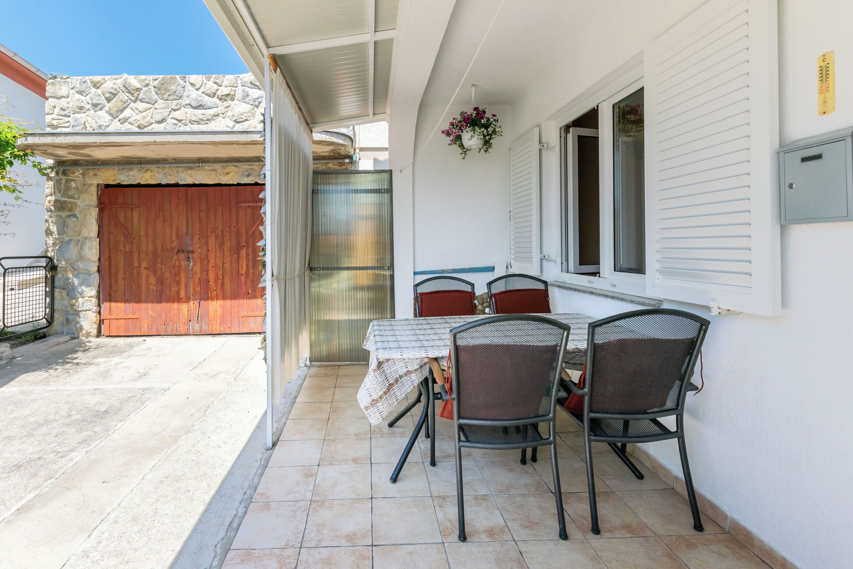 Eine Terrasse mit Tisch und Stühlen, eine Steinmauer, eine Holztür und ein blumengeschmückter Korb.