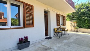 A building with wooden shutters, a concrete patio, and a potted plant. - Apartment Bosiljak (Jelsa)