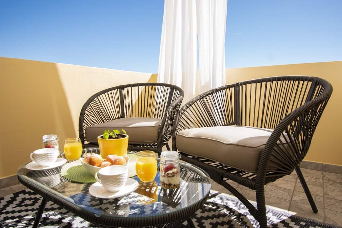 Ein Balkon mit Korbstühlen, einem Glastisch und Frühstücksgebäck, mit freier Sicht auf den Himmel.