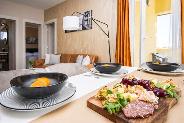 Une chambre d’hôtel moderne dotée d’un coin repas où est servi un copieux petit-déjeuner comprenant des fruits, du fromage et de la charcuterie.