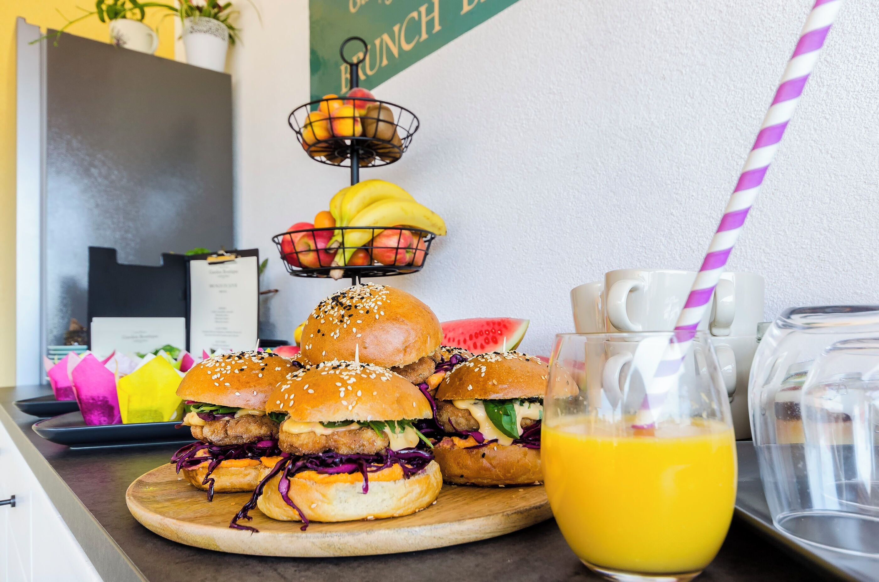 A breakfast setup with sandwiches, a fruit basket, and a pitcher of orange juice.