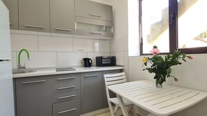 Une cuisine moderne avec des meubles gris, un plan de travail blanc, un évier, une machine à café noire et une fenêtre donnant sur un paysage verdoyant.