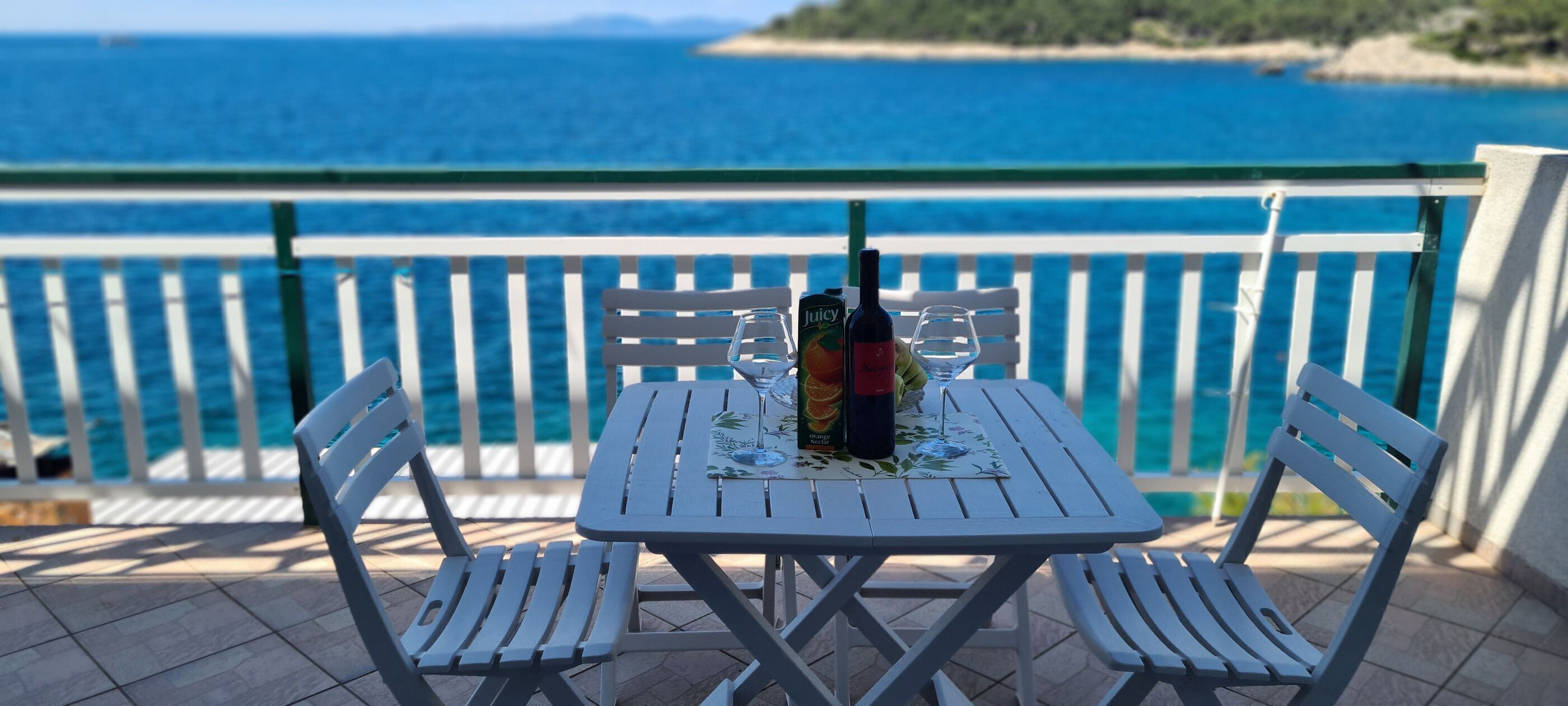 A table and chairs on a balcony with a view of the sea.