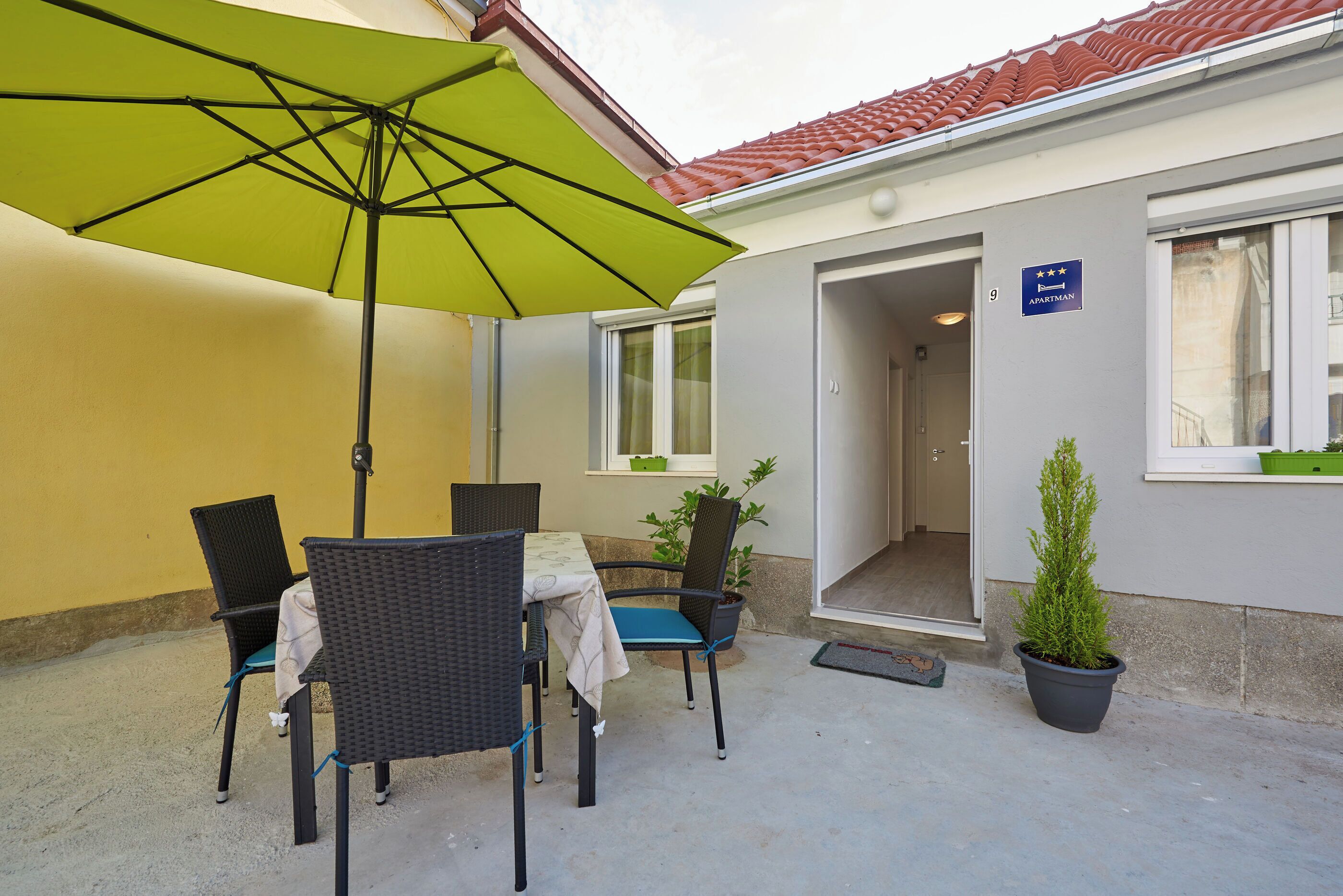 A patio with a table and chairs, a green umbrella, and a potted plant.