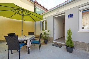 An outdoor patio with a table and chairs, a green umbrella, and potted plants. - House Dvor (Seget)