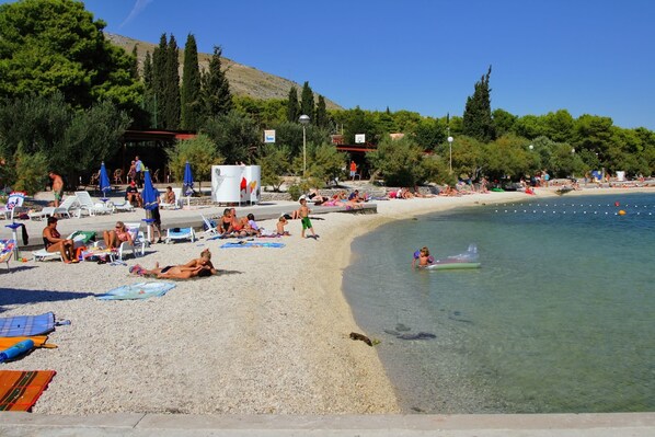 A beach with clear water, sun loungers, umbrellas, and people relaxing. - House Dvor (Seget)