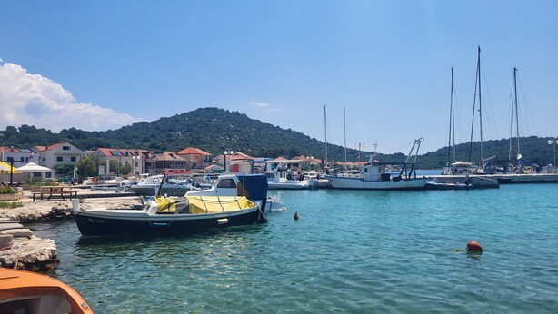 A marina with boats docked, a rocky shore, and buildings in the background. - Apartment Paradise (Sibenik)