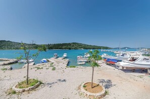 Una marina con diverse imbarcazioni ormeggiate, circondata da una spiaggia sabbiosa e qualche albero.