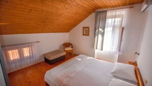 Ein Schlafzimmer mit Holzboden, einem Bett, einem Sessel und einem Fenster mit Vorhängen.