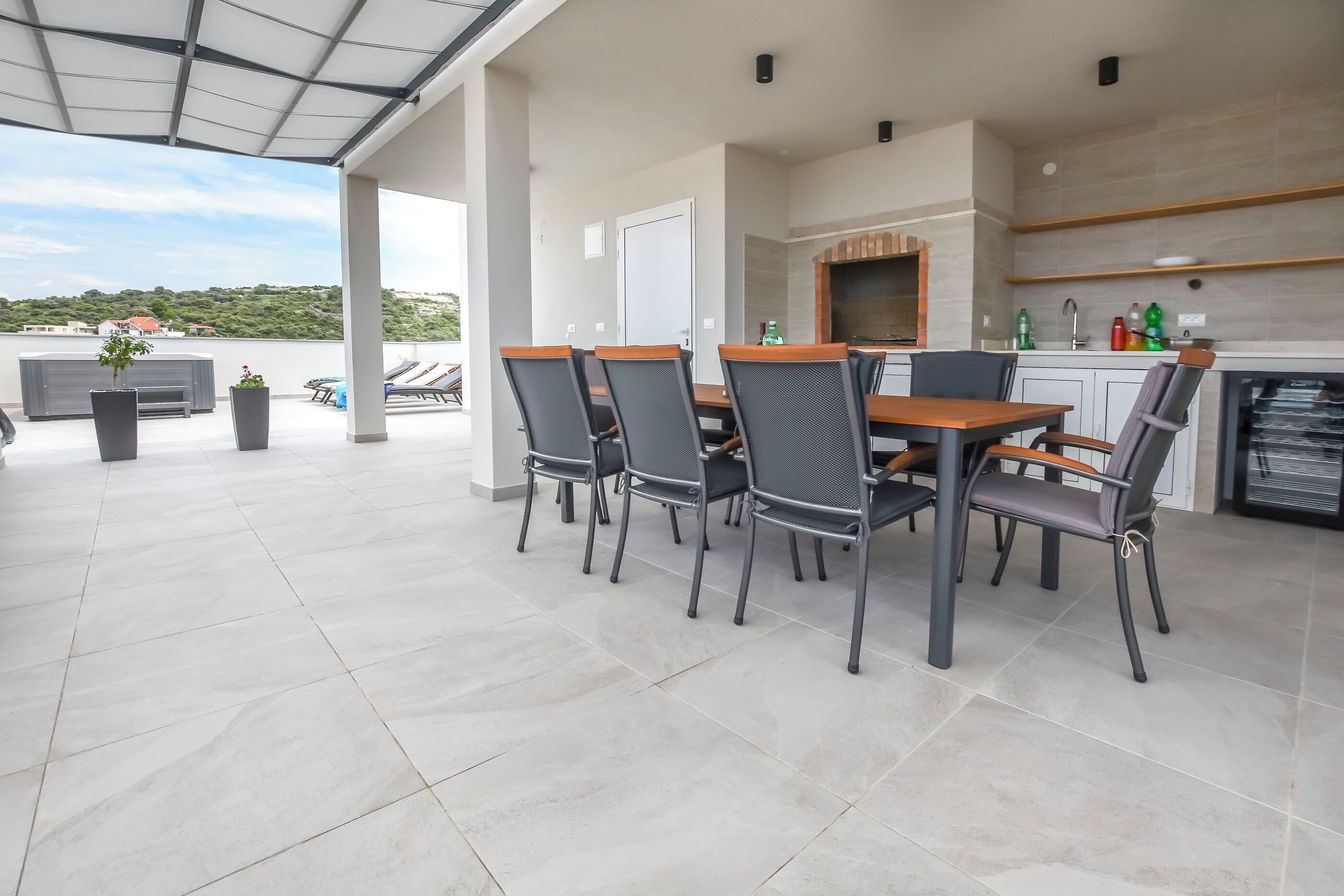 A covered outdoor dining area with a table and chairs, a kitchen with a stone backsplash, and a view of the landscape.