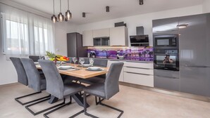 A modern kitchen with a dining area, featuring a large refrigerator, built-in oven, and a dining table set with chairs. - Apartment Sea Heaven (Rogoznica)
