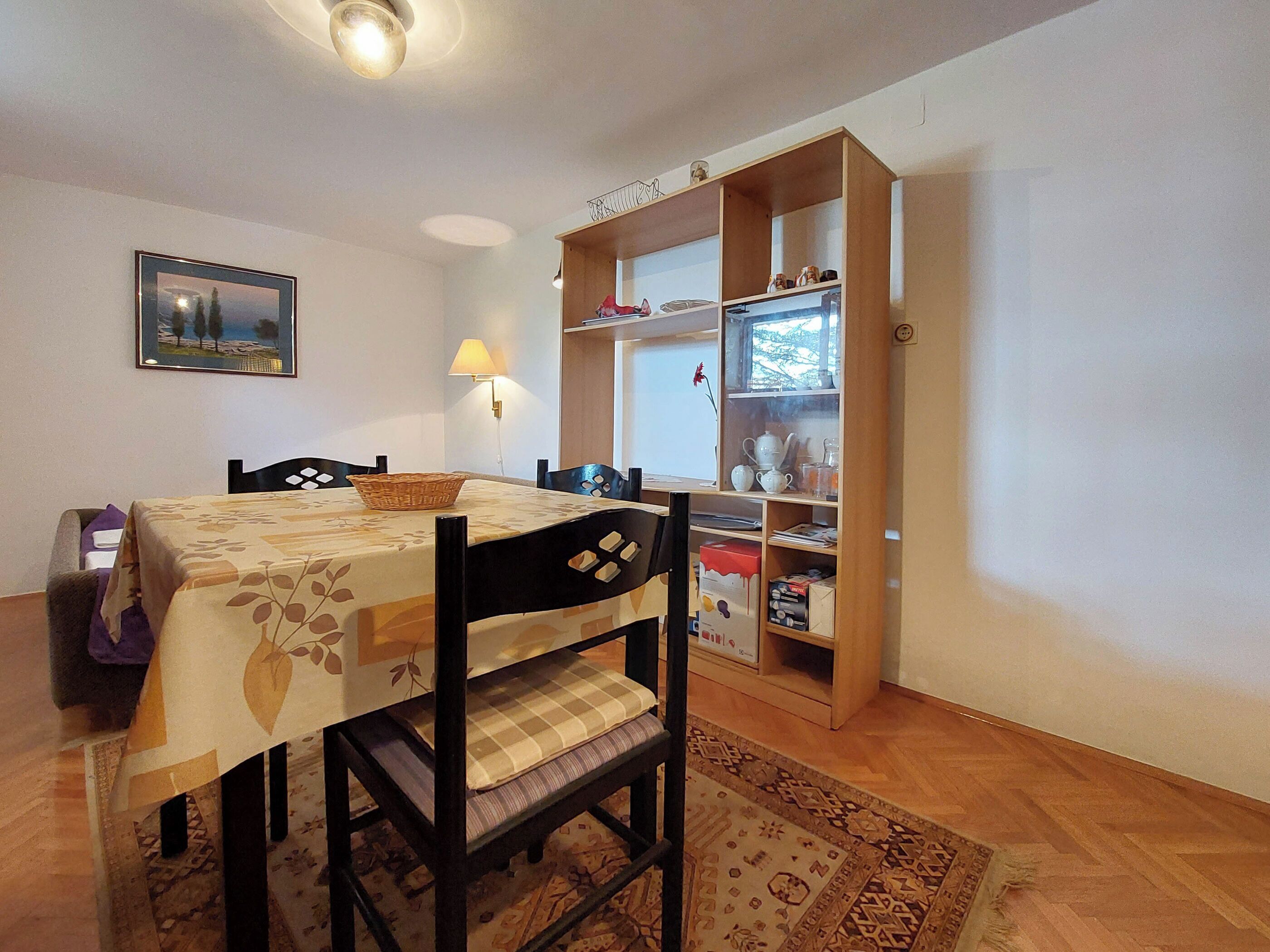 A dining area with a table set for two, a lamp, and a bookshelf with various items.
