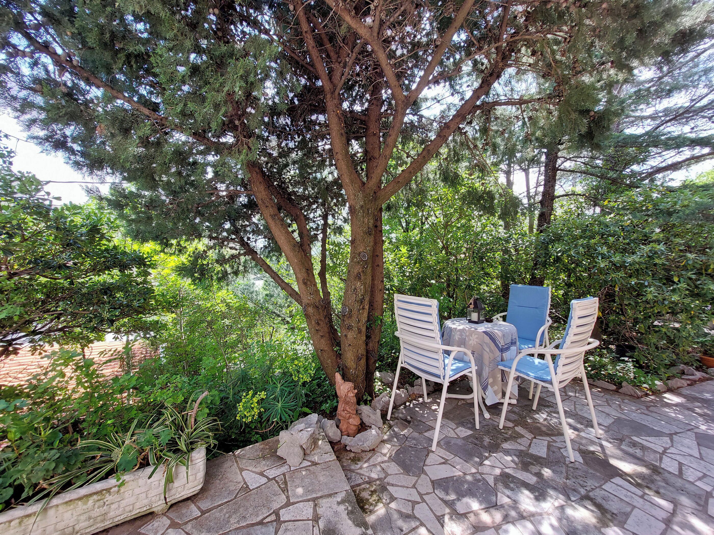 A patio with stone flooring, two white chairs with blue cushions, and a table.