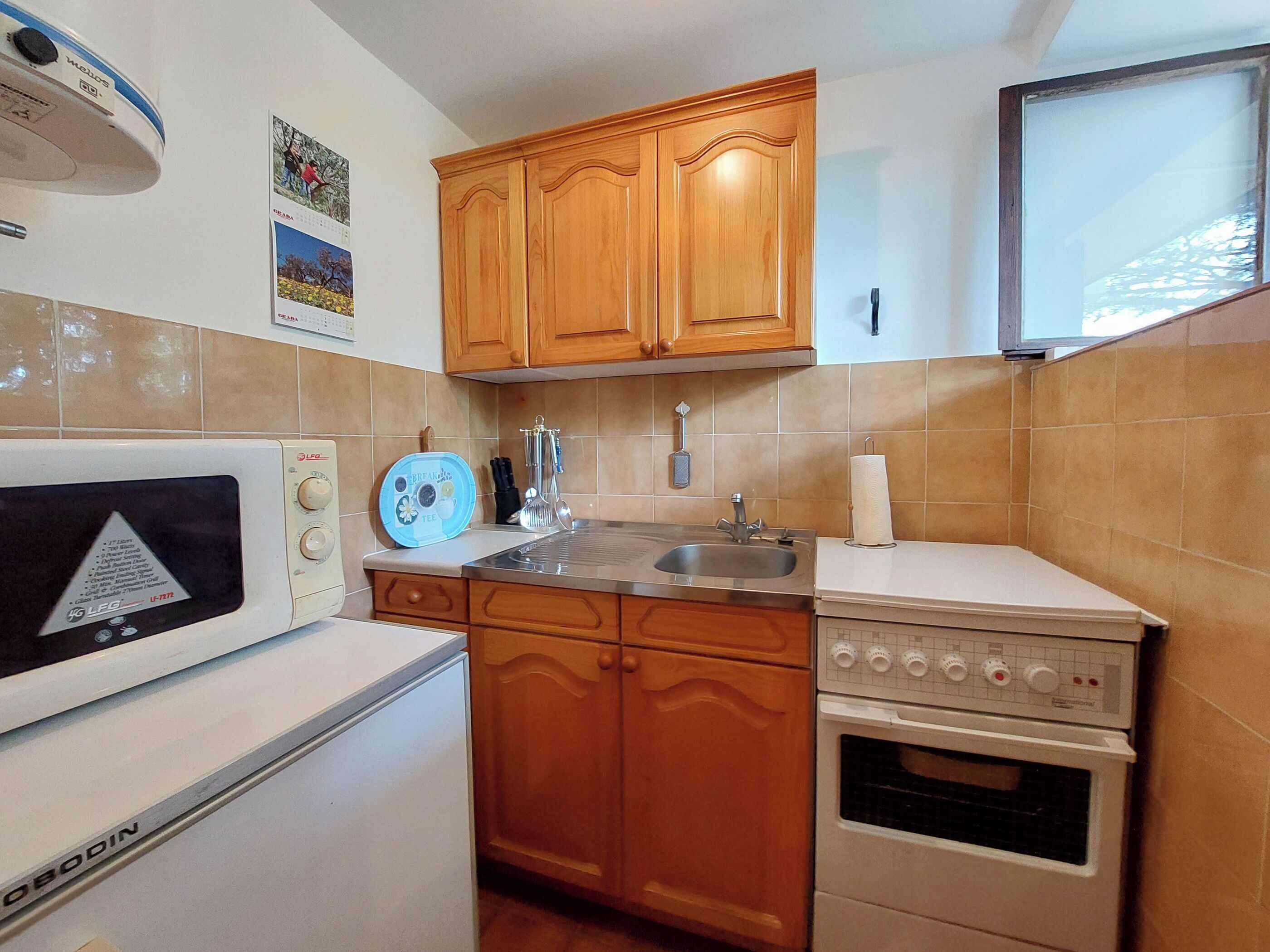 Une cuisine de taille réduite, dotée de meubles de rangement en bois, d’un four à micro-ondes, d’une cuisinière et d’un évier.