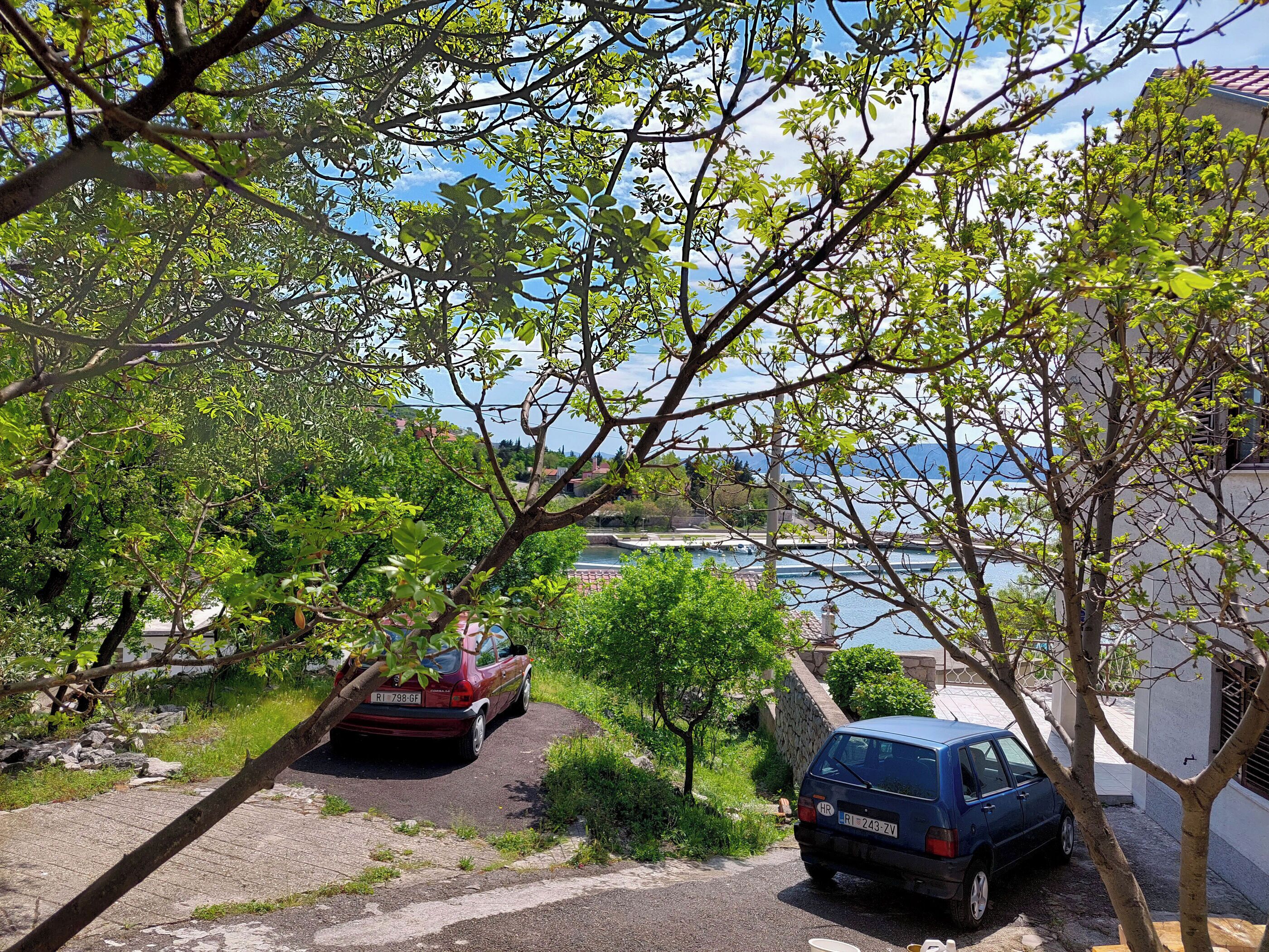 Un quartier résidentiel avec deux voitures garées, un mur de pierre et une vue sur une étendue d’eau.