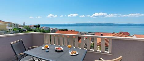 A balcony with a table set for breakfast, overlooking a coastal town and sea.