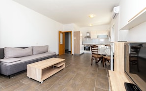 A modern apartment with a grey sofa, a wooden coffee table, a dining area with a table and chairs, and a kitchen with white cabinets and a stove. - Apartments Danijela (Dugi Rat)