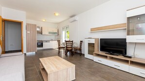 Una cocina moderna con armarios blancos, un comedor con sillas de madera, un televisor sobre un mueble de madera y un sofá.